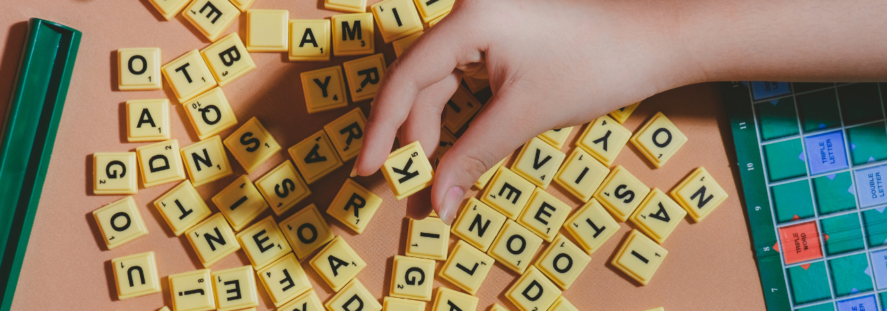 Scrabble tiles scattered against pink background with hand picking up letter k