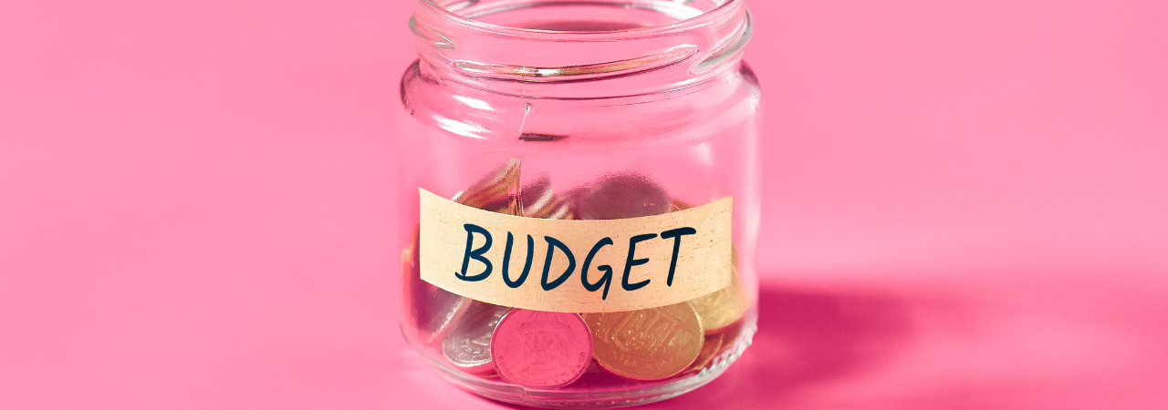 Money jar containing coins with label saying 'budget' against pink background