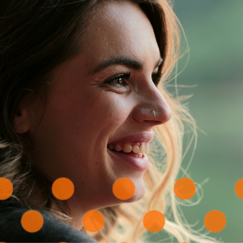 Woman with nose ring smiles towards something off camera, with funky orange dots overlay